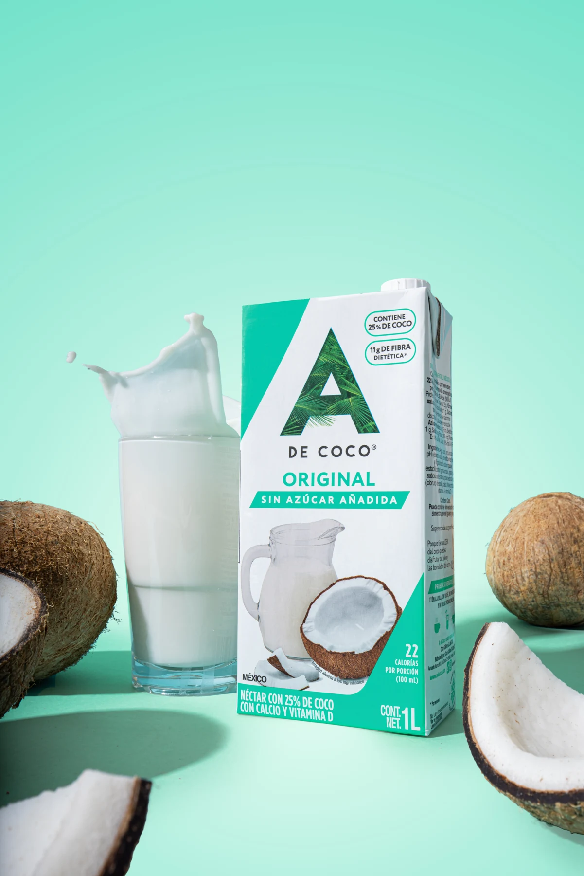 Néctar Original A de Coco junto a un vaso de bebida de coco y cocos frescos sobre un fondo verde menta