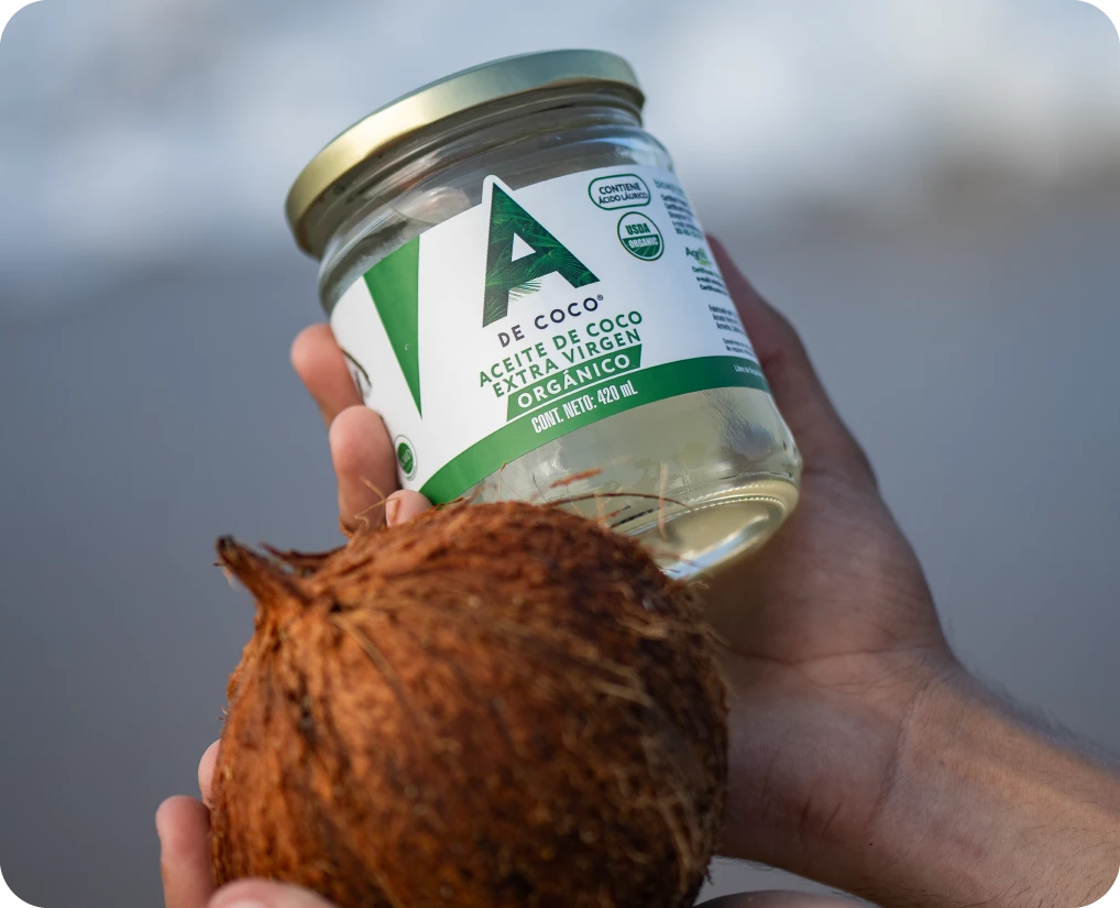 Aceite de coco extra virgen orgánico A de Coco sostenido junto a un coco
